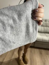 Sweater gris de tejido de punto grueso, con cuello alto, mangas anchas y aberturas laterales.