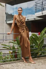 Vestido midi color marrón de satén, con cuello halter fluido y espalda descubierta. Presenta un nudo en la parte delantera, abertura frontal y cierre trasero con cremallera oculta.