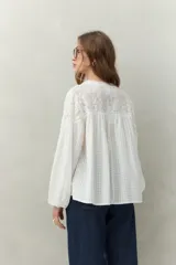 Blusa blanca de algodón con encaje floral en la parte superior, mangas largas abullonadas y escote con lazo.
