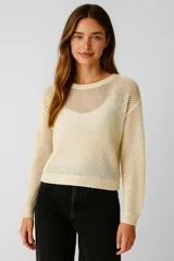 Sweater de punto calado color crema, de manga larga y cuello redondo a la base, con calce holgado.