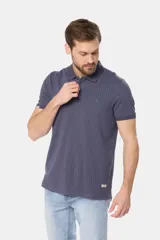 Polo de piqué color azul oscuro con un mini estampado geométrico repetitivo en todo el cuerpo. Presenta cuello y tapeta de botones en color liso, y un pequeño logo bordado en el pecho.