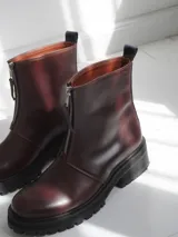 Botas de cuero color marrón con suela track negra y cierre frontal con cremallera roja.