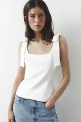 Top blanco de tejido elástico con escote cuadrado y tirantes anchos con lazos decorativos.