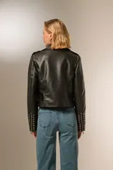Chaqueta corta de eco cuero negra con tachas plateadas, cuello camisero y cierre frontal con cremallera.
