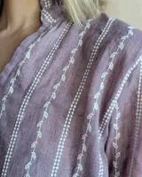 Blusa color beige con cuello con volados, mangas largas abullonadas con puños elásticos y cierre con botones en la parte delantera.