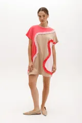 Vestido corto de algodón con diseño de bloques de color en coral, beige y rosado claro. Presenta un corte relajado, cuello redondo, mangas cortas tipo raglán y detalles de volados ondulados que dividen las secciones de color.