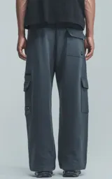 Pantalón de jogging gris oscuro, de corte amplio, con cintura y puños elásticos, bolsillos laterales y trasero, y bolsillo lateral adicional con cierre.
