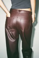 Pantalón marrón de tiro medio con trabillas en la cintura, cinco bolsillos y pernera ancha. Cierre frontal con cremallera, botón oculto y gancho metálico.