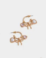 Aros dorados tipo argolla con dijes colgantes de corazón de perla, corazón de strass rosa y moño dorado.