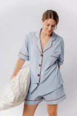 Pijama de algodón color celeste, compuesto por una camisa de manga corta con botones marrones y ribetes festoneados en color marrón, y un short con elástico en la cintura y ribetes festoneados en el ruedo.
