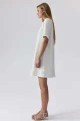 Vestido corto blanco de corte evasé, con cuello redondo y manga corta. Presenta abertura de cerradura con botón oculto en la nuca.