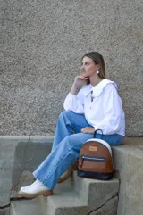 Mochila de cuero color tostado, con base y espalda en negro y tapa superior en blanco. Tiene un bolsillo frontal con cierre y un pequeño aplique de cuero con el logo de la marca.