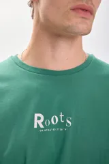 Remera verde con estampa frontal de la marca Roots en color blanco. Corte oversize y mangas cortas.