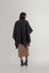 Ruana de tejido de punto grueso color gris oscuro con flecos en el borde inferior. Presenta apliques de lana en forma de líneas onduladas en color negro, fucsia, amarillo y celeste.