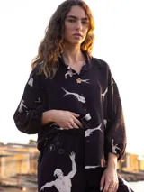 Camisa negra con estampado de figuras humanas blancas, cuello clásico, cierre frontal con botones y mangas 3/4 con lazos ajustables en los puños.