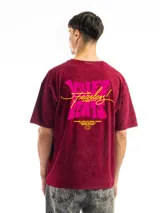 Remera oversize de algodón con efecto acid wash en color rojo oscuro/bordó. Presenta un pequeño estampado en el pecho con texto en color rosa y amarillo.