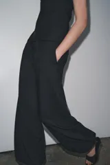 Pantalón de tiro medio confeccionado en hilatura con mezcla de viscosa, color negro. Presenta bolsillos laterales ocultos en costura, bajo acabado en puño con botones y cierre frontal con cremallera, botón y ganchos metálicos.