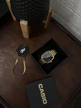 Reloj Casio Quartz dorado con caja cuadrada, dial negro y pulsera de eslabones.