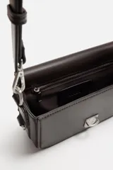Bandolera marrón de cuero sintético con correa ajustable y extraíble. Tiene cierre metálico y bolsillo interno con cremallera.