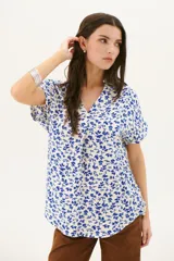 Blusa estampada con hojas azules sobre fondo blanco, con cuello en V y mangas cortas con dobladillo.