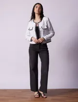 Chaqueta de tweed blanca con ribete negro, escote a la base, abertura central con botones, bolsillos delanteros y puños con aplique de botones perlados.