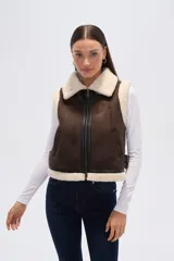 Chaleco sin mangas de eco-cuero marrón con forro y cuello de piel sintética color crema. Presenta cierre frontal y detalles de hebillas ajustables en los laterales.