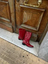 Bota de cuero vacuno color rojo, de caña alta y punta fina, con detalles de tiras con hebillas plateadas. El interior está forrado en cuero vacuno. Tiene un fondo de doble vira de madera.