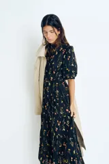 Vestido largo de algodón negro con estampado de flores pequeñas en tonos rosa y amarillo. Tiene cuello mao, mangas globo cortas, cinturón fino extraíble y falda acampanada con fruncido escalonado.