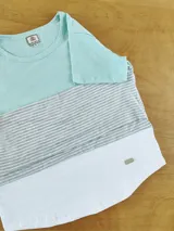 Remera de manga corta con diseño de bloques de color: celeste en la parte superior, a rayas horizontales grises y blancas en el medio y blanco en la parte inferior.