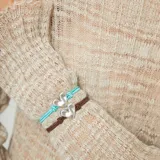 Pulsera ajustable de hilo elástico marrón, con un dije central de corazón plateado de forma orgánica y un cierre magnético plateado.