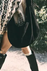 Bolso tipo hobo de gamuza negra, con forma holgada y cierre principal de cremallera. Se lleva al hombro con dos asas de correa delgadas sujetas con argollas metálicas plateadas.