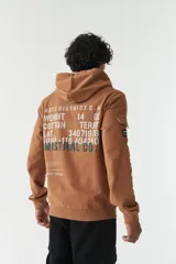 Campera marrón de felpa con capucha y cordón ajustable, lettering estampado en la espalda, bolsillo en la manga, puños y logo en grifa de goma.