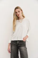 Remera blanca de algodón con calce relajado y cuello redondo. Tiene mangas largas que se ajustan hacia los puños.