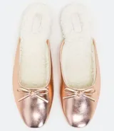 Zapatilla mule color rosa metalizado, con punta redonda, lazo decorativo en la parte superior, interior de piel sintética y suela plana.