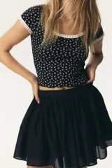 Top corto de manga corta, ajustado al cuerpo, con estampado floral pequeño en blanco sobre fondo negro. Presenta ribete de encaje blanco en el escote redondo y en los bordes de las mangas. El cuerpo principal parece ser de tejido acanalado.