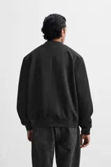 Cazadora bomber negra de corte regular, confeccionada en tejido con efecto ante. Cuenta con cuello, puños y bajo de rib elástico, bolsillos de vivo en la cadera y cierre frontal con cremallera.