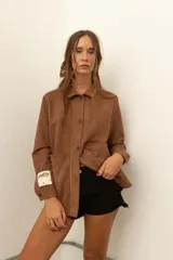 Camisa marrón de corte recto con cuello camisero, cierre frontal con botones, mangas largas con puños abotonados y bolsillos de parche en el pecho.