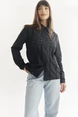 Camisa negra de manga larga con cuello clásico y cierre frontal con botones. Presenta detalles de encaje a lo largo del frente y en los puños.
