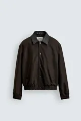 Cazadora de algodón con estructura canvas, color marrón oscuro, de corte relajado. Presenta cuello solapa de cuero negro, cierre frontal con botones a presión, bolsillos de vivo en cadera y puños y bajo elásticos.