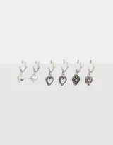 Set de tres pares de aros argolla plateados con dijes de corazones con diferentes diseños.