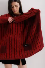 Sweater tejido de punto color fucsia con diseño de trenzas verticales en color naranja. Tiene cuello redondo y dos bolsillos frontales.