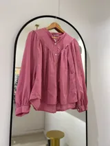 Camisa rosa de manga larga con puños, cuello mao y cierre frontal con botones. Tiene corte y frunce en la parte delantera.
