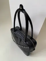 Cartera rígida negra de cuero con tachas plateadas y tres combinaciones de cuero diferentes que aportan textura. Tiene herrajes y cierre metálico plateado marca YKK. Cuenta con un asa fina para llevar al hombro o en la mano y una correa larga extra regulable.