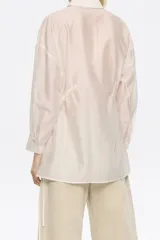 Camisa color crudo de corte ajustado en cintura, con cuello camisero, manga larga con puño y botón, cierre frontal con botonadura y túneles ajustables con tiras de tejido.