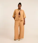 Pantalón pantalona color beige, de tiro alto, con cintura fija, trabillas, cierre tradicional, bolsillos, elástico trasero y cinturón con hebilla redonda.