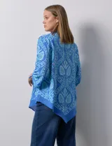 Blusa de gasa estampada marca Ruby Rd, de color azul. Tiene cuello a la base, escote en V y abertura central con botones. La delantera es plisada. Las mangas son ¾ con frunce. El ruedo y la espalda son asimétricos.