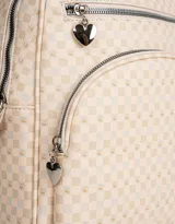 Mochila color crema con estampado geométrico de cuadros, confeccionada en cuerina. Tiene asa corta de mano, correas regulables, doble bolsillo frontal con cierre (uno con dije de corazón) y pouch lateral extraíble con cierre y dije de corazón.
