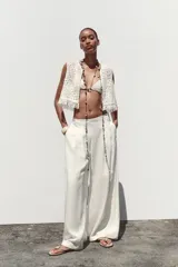Pantalón blanco de tiro alto con pinzas delanteras, bolsillos laterales y pernera ancha. Cierre lateral con cremallera oculta.