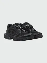 Zapatillas deportivas Diesel modelo S-Pro-V-Dense, color negro, con diseño robusto y estilo 'chunky' o 'dad shoe'. Presentan una combinación de malla transpirable y superposiciones de material sintético brillante. Los cordones son bicolores (negro y blanco).