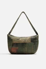 Bolso de hombro tipo bandolera con estampado de parches de denim en tonos verdes, marrones y azules. Tiene un compartimento principal con cierre de cremallera, un bolsillo interior con cremallera y un bolsillo trasero con cremallera. El asa de hombro es ajustable.